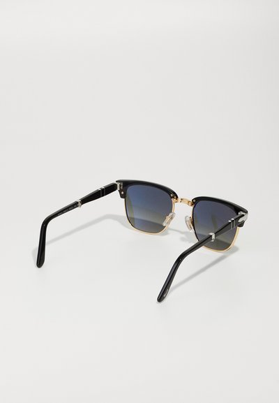 Black and gold sunglasses with dark lenses, cat-eye shape, metal accents, and clear nose pads. Features black temples with silver detailing.
