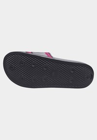 Svart gummislip-on sandal med en texturerad gripmönster och distinkta cirkulära gummiknobb för grepp; accentuerad med rosa ränder.