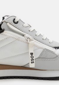 Šedá a bílá sportovní bota s texturovaným nylonovým svrškem, kontrastními detaily, zipovým uzávěrem a černou gumovou podrážkou. Obsahuje tag "BOSS".