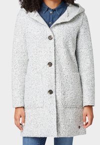 Šedý texturovaný kabát s kapucí, který má velké knoflíky, dvě přední kapsy a pletený detail na límci. Vzhled je po kolena.