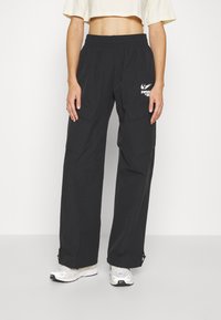 Pantalones cargo negros con una cinturilla elástica, bolsillos laterales prominentes y un pequeño detalle del logo blanco en la parte delantera. Ajustes en el tobillo.