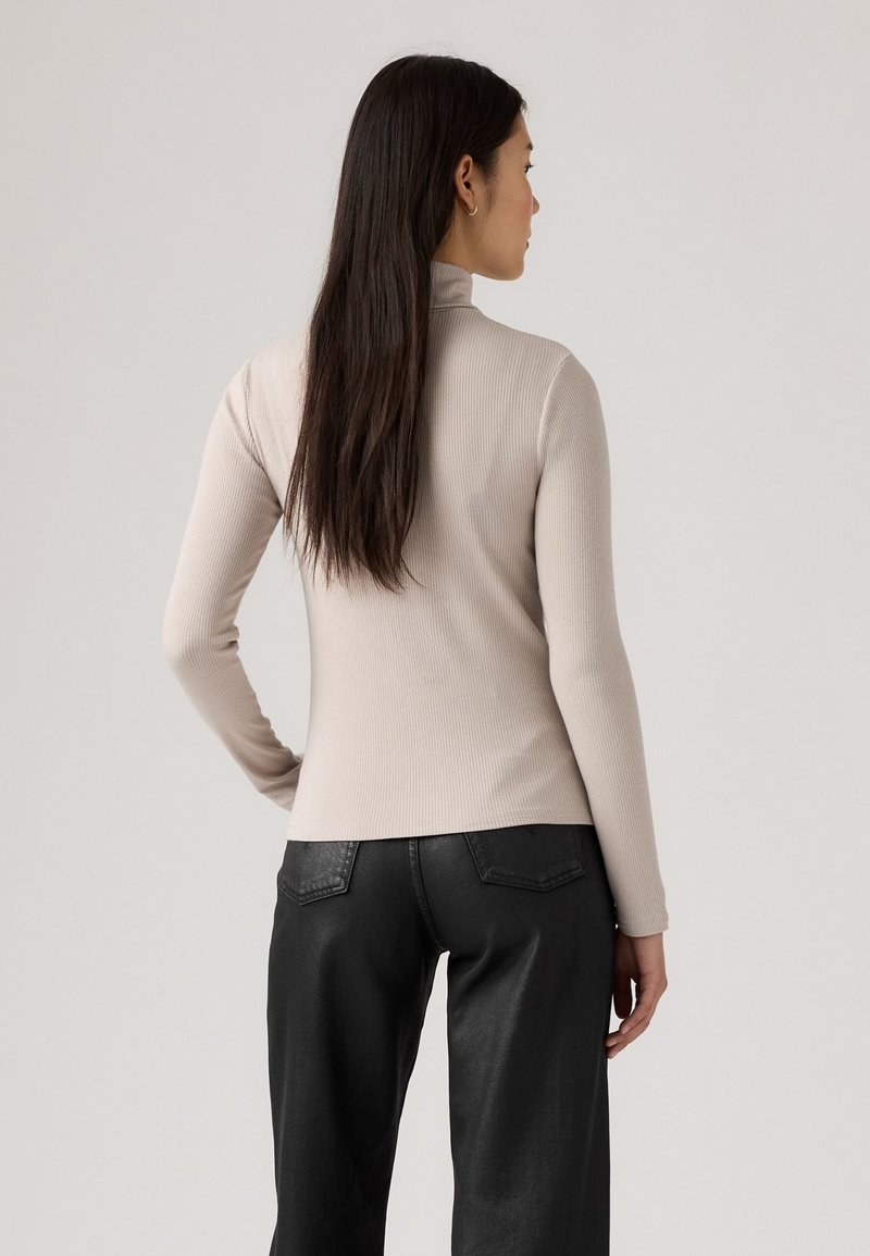 Hellbeige gerippter Rollkragenpullover mit langen Ärmeln, taillierter Silhouette und weichem Stoff, kombiniert mit schwarzen, hochgeschnittenen Hosen.