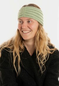 Jasnozielona dziana opaska na głowę z teksturowanymi paskami. Noszona przez osobę z długimi włosami, na białym tle.