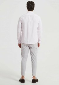 Chemise à manches longues rose clair avec un col, associée à un pantalon gris clair ajusté, portée avec des chaussures foncées. Texture du tissu lisse visible.