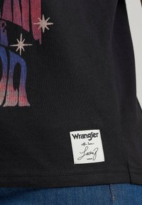 Camiseta de algodón negra con un estampado gráfico colorido, motivos de estrellas y una etiqueta tejida blanca con el nombre de la marca y su firma.