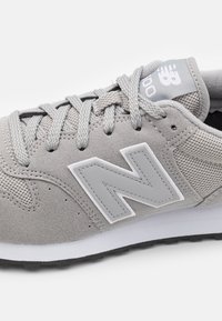 Sneaker in suede grigio con accenti in mesh, dotato di lacci grigi e un logo bianco. Suola in gomma sottile con una leggera texture.