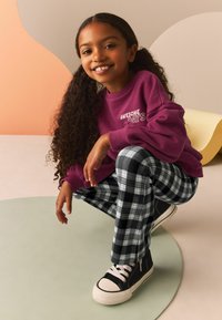 Fioletowy polarowy sweatshirt z napisem "NIESAMOWITE DNIE", w połączeniu z czarnymi i białymi spodniami w kratę oraz czarnymi sneakersami z białymi akcentami.