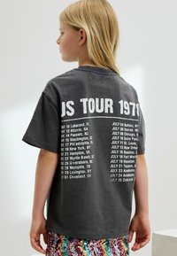 Szara bawełniana koszulka z krótkim rękawem, z tekstem "U.S. TOUR 1978" oraz datami miast nadrukowanymi na białym tle z tyłu. Luźny krój, gładki przód.