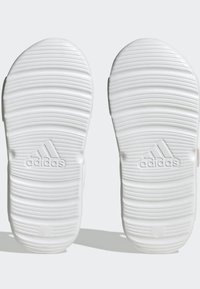 Suole delle scarpe bianche Adidas con scanalature testurizzate e un logo sottile. Il design presenta una forma liscia e arrotondata con uno spessore uniforme in tutto.