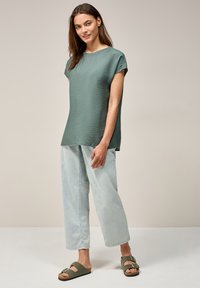 Top corto a maniche corte verde chiaro con texture, abbinato a pantaloni in denim blu chiaro larghi e sandali verde scuro con fibbie. Design semplice e moderno.
