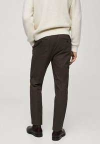 Braune maßgeschneiderte Hosen mit strukturierter Oberfläche, ausgestattet mit zwei Gesäßtaschen und einem schlanken Schnitt, kombiniert mit einem cremefarbenen Strickpullover.