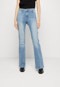 Jeans flare azzurri chiari realizzati in denim, con una vita a media altezza, cinque tasche e cuciture a contrasto. Texture liscia con zone sbiadite.