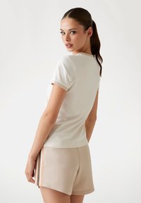 Witte T-shirt met korte mouwen en een ronde hals, gecombineerd met beige shorts met zijsstripes en een gladde, textuurvolle stof.
