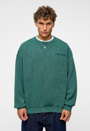 Groene oversized sweatshirt met een ronde hals en geribde manchetten. Voorzien van een subtiel logo-detail op de voorkant. Zacht, textuur-stof.