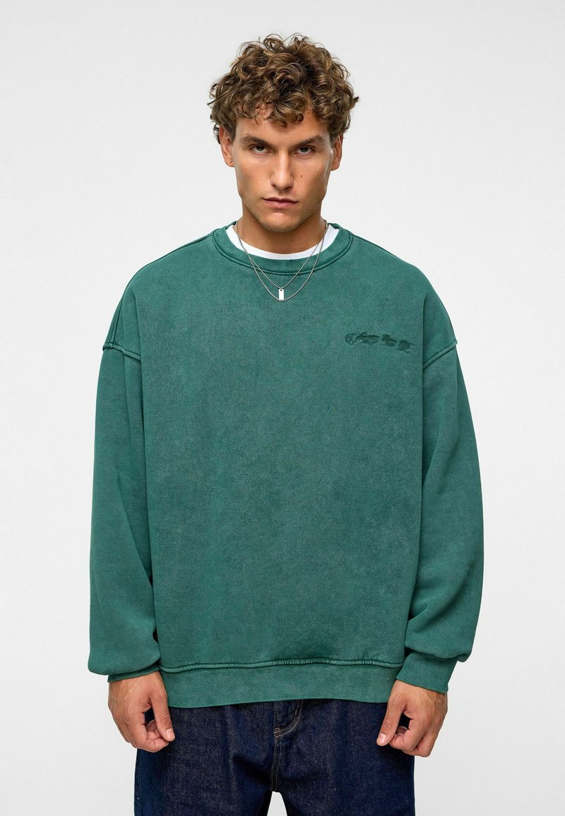 Groene oversized sweatshirt met een ronde hals en geribde manchetten. Voorzien van een subtiel logo-detail op de voorkant. Zacht, textuur-stof.