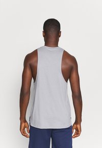 Camiseta sin mangas gris con escote redondo y brazos anchos, hecha de una tela suave, combinada con pantalones cortos azules, mostrando un estilo casual.