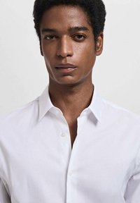 Camisa blanca de botonadura clásica con cuello, hecha de una tela lisa, con un corte entallado y sin patrones visibles.