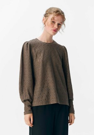 Brun broderad blus med långa puffärmar och rund halsringning. Har ett intrikat diamantmönster och textuerad tyg. Avslappnad passform.