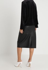 Czarna welurowa bluzka z długim rękawem oraz czarna skórzana midi spódnica z rozcięciem z tyłu, w połączeniu z białymi czółenkami z ostrym noskiem.