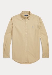 Beige skjorta med knappar gjord av bomull, med krage, långa ärmar och en liten blå logotyp på vänster bröst.