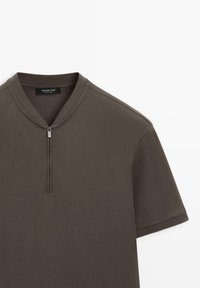 Olivenfarvet skjorte med korte ærmer, halv lynlås og ribbet krave, vist fladt mod en hvid baggrund.