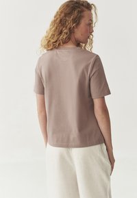 Tričko s krátkým rukávem a kulatým výstřihem v světle mauve barvě, vyrobené z bavlny, s uvolněným střihem, rovním lemem a minimálním šitím.