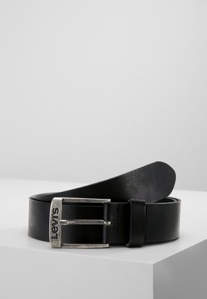 Zwarte leren riem met zilverkleurige metalen gesp gegraveerd met "Levi's", opgerold en geplaatst op een wit oppervlak tegen een grijze achtergrond.