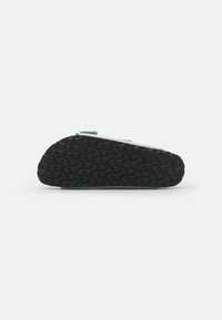 Green slip-on shoe with a textured black rubber sole featuring a wave pattern, designed for comfort and ease of wear.