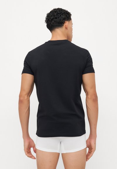 Schwarzes T-Shirt mit kurzen Ärmeln und Rundhalsausschnitt, aus glattem Stoff gefertigt. Die Person trägt weiße Boxer-Shorts, die eine figurbetonte Silhouette zeigen.