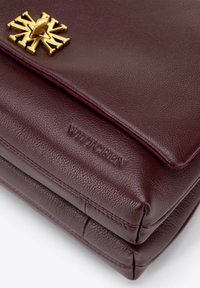 Bordó kožená kabelka se zlatou kováním, s hleděným designem, raženým logem a viditelnými detaily šití.