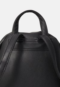 Sac à dos en cuir noir avec une texture granuleuse, doté de deux poignées et de sangles réglables. Design simple avec une forme épurée.