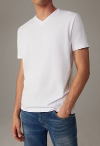 Weißes Baumwoll-T-Shirt mit V-Ausschnitt, kurzen Ärmeln und lockerer Passform, kombiniert mit blauen Jeans aus Denim mit leichtem Wasch-Effekt.