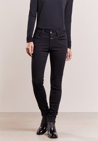 Jeans in denim nero con un fit slim, dotati di tasche frontali, chiusura con bottone e una texture liscia e morbida. Indossati con un top a maniche lunghe.