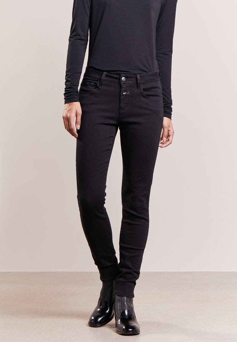 Jeans in denim nero con un fit slim, dotati di tasche frontali, chiusura con bottone e una texture liscia e morbida. Indossati con un top a maniche lunghe.