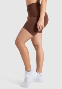 Bruna högmidjade cykelshorts i elastiskt material, med en slät yta och figurnära design, samt vita träningsskor och strumpor.