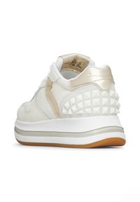 Sneaker bianca con un superiore testurizzato, accenti dorati metallici e un retro decorato con borchie a piramide. Suola spessa bianca con battistrada in gomma color cuoio.