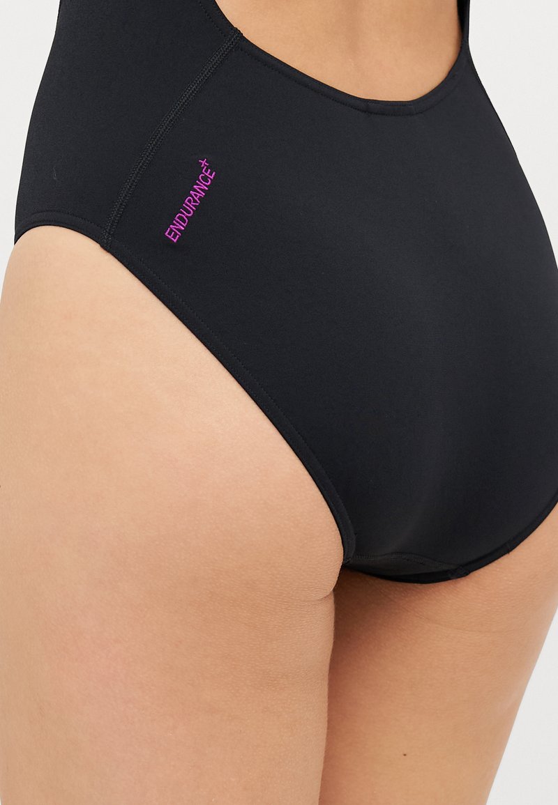 Schwarze Schwimmhose aus dehnbarem Material. Verfügt über einen hohen Bund und ein dezentes ENDURANCE+ Logo in Pink an der Seite. Glatte Textur, keine Muster.