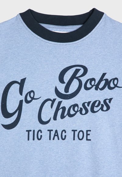 Camiseta de manga corta azul claro con texto negro que dice "Ve Bobo Choses TIC TAC TOE", con un cuello redondo negro.
