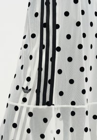 Λευκό διάφανο ύφασμα με μαύρες πουά, τρεις κατακόρυφες μαύρες ρίγες και μικρό μαύρο λογότυπο Adidas trefoil.