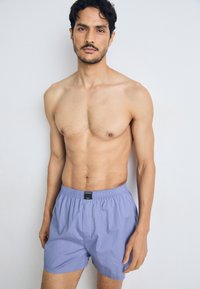 Vīriešu gaiši violets kokvilnas bokseršorti ar elastīgu jostu un logo birku, kas piedāvā brīvu piegriezumu un gludu tekstūru.