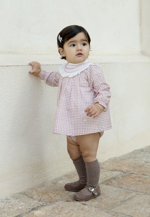 Vestido de cuadritos rosas con cuello blanco con volantes, combinado con zapatos marrones y calcetas marrones hasta la rodilla. Tejido suave, diseño divertido y líneas limpias.