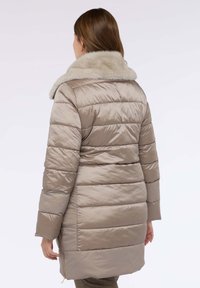 Béžový prošívaný kabát s horizontálním prošíváním a límcem z umělé kožešiny. Hladká, lesklá látka a zipové kapsy na bocích. Středně dlouhý střih.