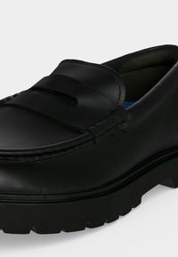 Μαύρο δερμάτινο loafer με χοντρή σόλα τύπου lug, διακοσμητικό λουράκι πάνω από το άνω μέρος και λεπτομερή ραφή κατά μήκος των άκρων.