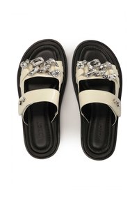 Sandali a due listini con cinturini in pelle sintetica crema, suole in gomma nera e una catena decorativa in argento con gemme trasparenti sopra.