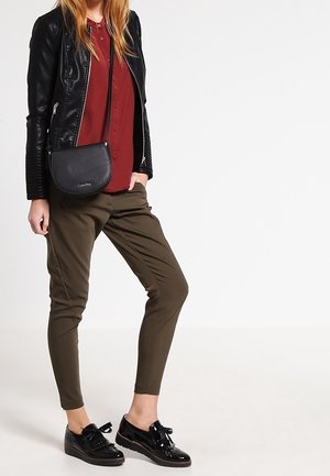 Černá kožená bunda, vínová košile s knoflíky, olivově zelené zúžené kalhoty a černé lakované boty s mašlemi, doplněné černou krosnou.