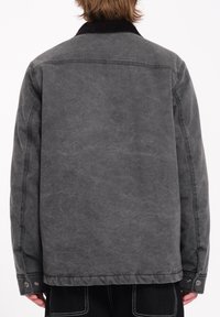 Veste en denim gris avec un col en velours côtelé, présentant une coupe décontractée, des poches latérales et des coutures visibles le long de l'ourlet et des manches.