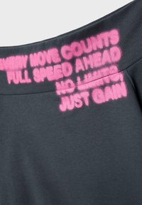 Tissu gris foncé avec texte en rose vif pochoir en spray sur une ceinture côtelée, mots partiellement lisibles incluant "FULL SPEED AHEAD" et "JUST GAIN".