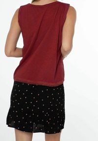 Top senza maniche color bordeaux con rifiniture all'uncinetto; abbinato a una gonna nera con motivi floreali sparsi e orlo arricciato.