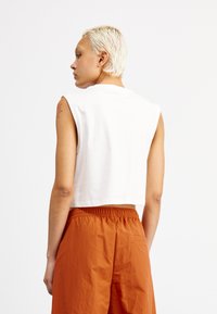 Top sin mangas recortado blanco, de material de algodón. Combinado con shorts sueltos naranjas que cuentan con una cintura elástica y bolsillos laterales.