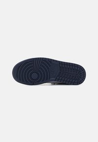 Semelle de basket Nike bleu foncé avec motifs circulaires et en grille visibles sur fond blanc uni.